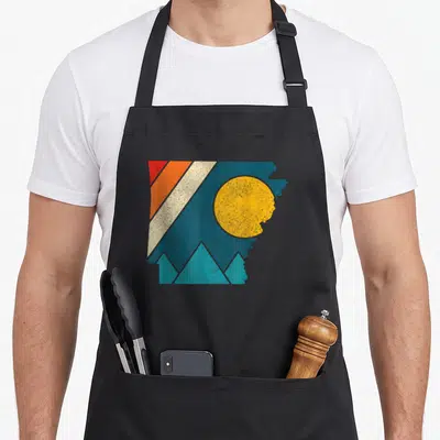 Arkansas pride apron - Retro Arkansas state outline with sun, teal mountains, and diagonal stripes in yellow, red — shown on a black cotton canvas apron against a white background