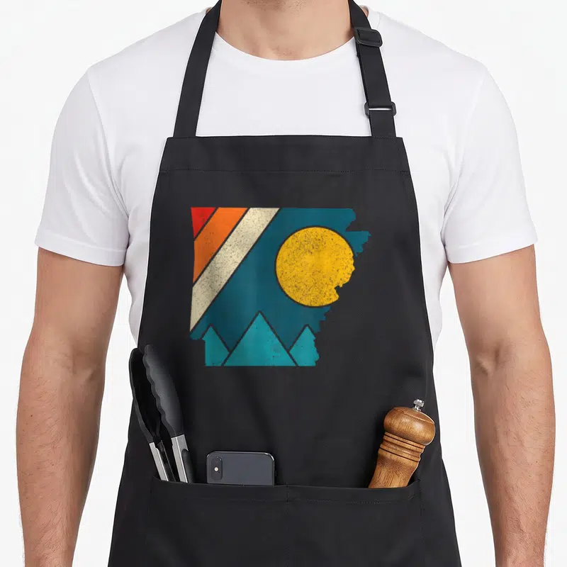 Arkansas pride apron - Retro Arkansas state outline with sun, teal mountains, and diagonal stripes in yellow, red — shown on a black cotton canvas apron against a white background
