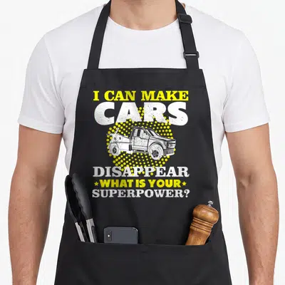 Service truck apron - Tow truck over yellow halftone circle with text I can make cars disappear — shown on a black cotton canvas apron against a white background