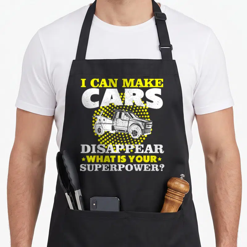 Service truck apron - Tow truck over yellow halftone circle with text I can make cars disappear — shown on a black cotton canvas apron against a white background
