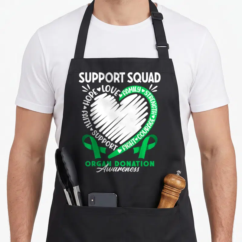 Support organ apron - White heart surrounded by support words and two green ribbons for organ donation — shown on a black cotton canvas apron against a white background