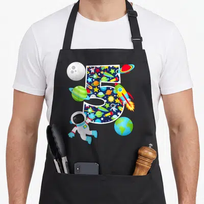 System birthday apron - Number 5 filled with space pattern surrounded by astronaut rocket and planets in cartoon style — shown on a black cotton canvas apron against a white background