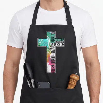 Music jesus christian apron - Typographic cross formed by music and Jesus text over watercolor notes in white green — shown on a black cotton canvas apron against a white background