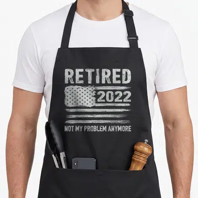 Retired american flag apron - White distressed USA flag with Retired 2022 Not My Problem Anymore text — shown on a black cotton canvas apron against a white background
