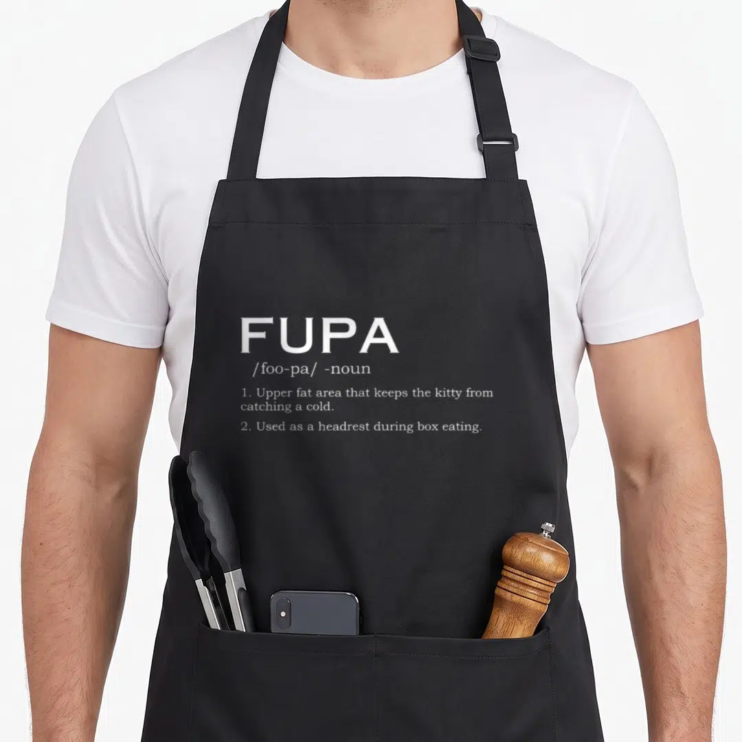 Definition fat man in apron - White typography defining FUPA as a cat headrest and cold preventer on dark fabric — shown on a black cotton canvas apron against a white background