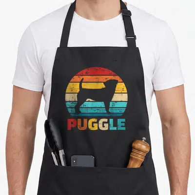 Vintage puggle apron - Grey dog silhouette inside red orange yellow beige teal blue striped circle with PUGGLE text — shown on a black cotton canvas apron against a white background