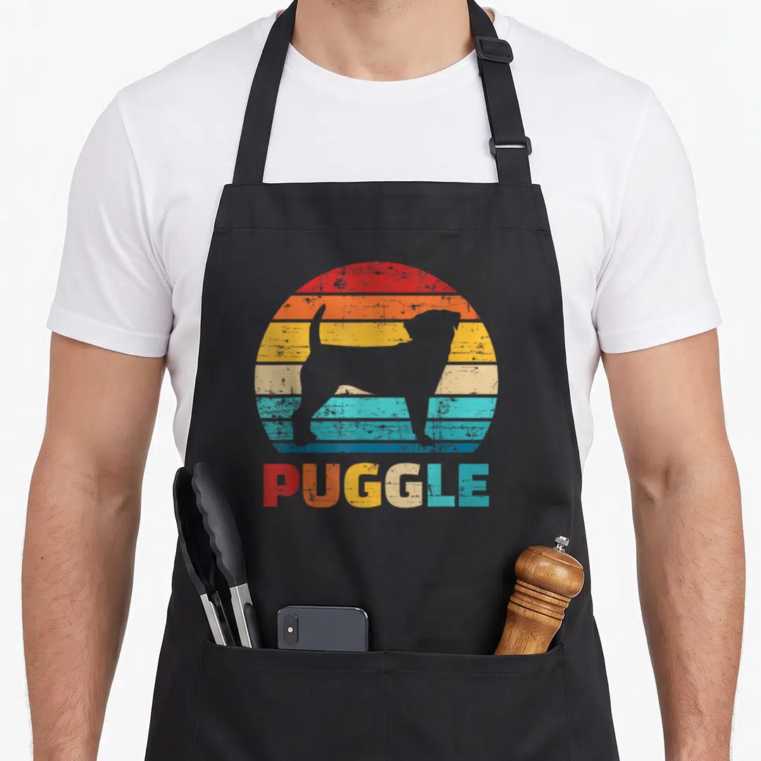 Vintage puggle apron - Grey dog silhouette inside red orange yellow beige teal blue striped circle with PUGGLE text — shown on a black cotton canvas apron against a white background