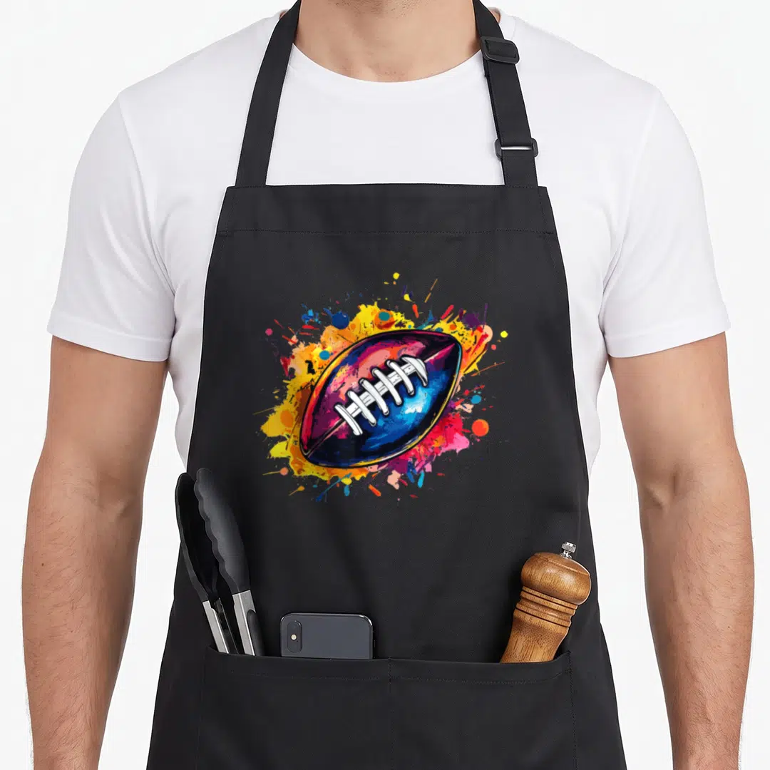Game player football apron - Colorful cartoon American football on blue, yellow, red, and purple paint splatters — shown on a black cotton canvas apron against a white background