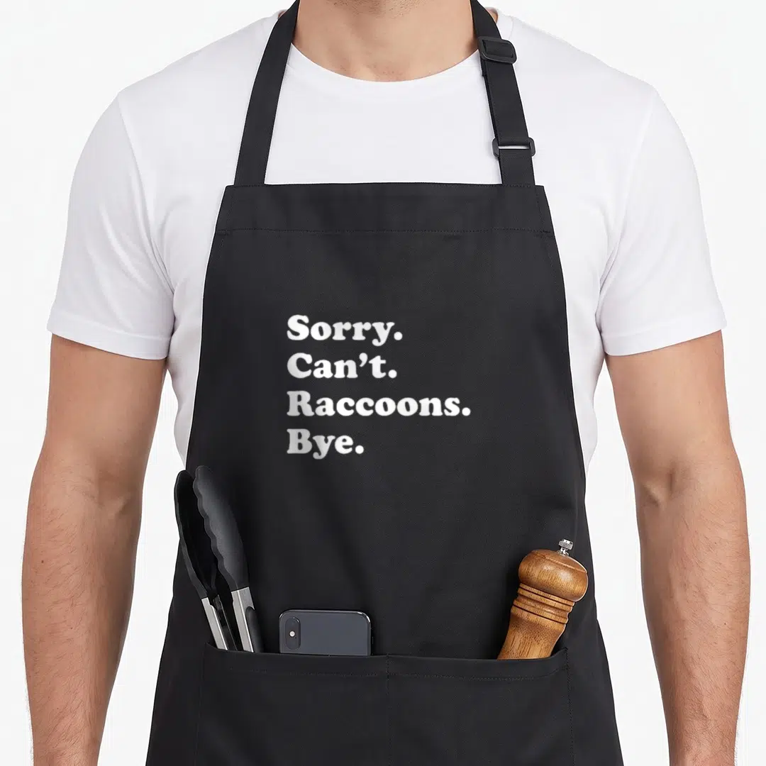 Raccoon apron or apron - White stacked text reading Sorry Can't Raccoons Bye on gray background — shown on a black cotton canvas apron against a white background