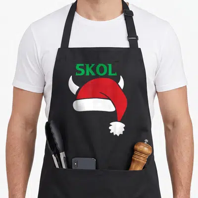Santa scandinavian aprons - Green SKOL text above red and white santa hat with two white horns — shown on a black cotton canvas apron against a white background