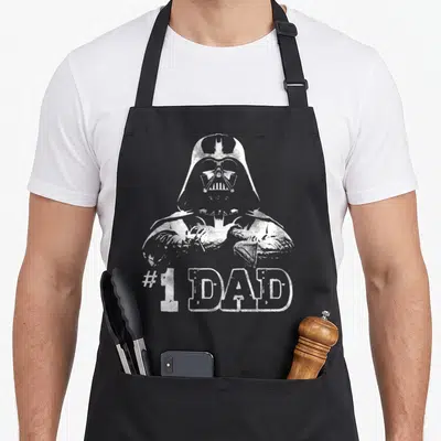 Faded father day apron - Distressed white Darth Vader graphic above #1 DAD text — shown on a black cotton canvas apron against a white background