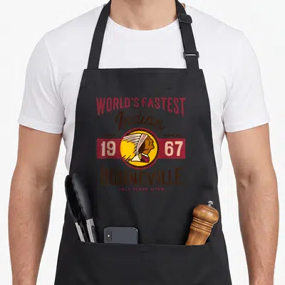 Utah motorcycle apron - Burt Munro 1967 Bonneville vintage logo with Native American head profile and stacked text — shown on a black cotton canvas apron against a white background