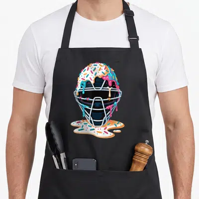 Catcher ice cream apron - Black catcher mask covered in dripping white pink blue icing and multicolored sprinkles — shown on a black cotton canvas apron against a white background