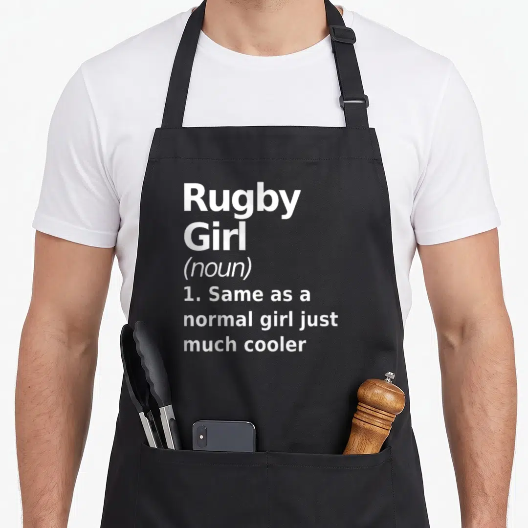 Rugby sassy apron - White stacked text defining rugby girl as normal but cooler on gray background — shown on a black cotton canvas apron against a white background