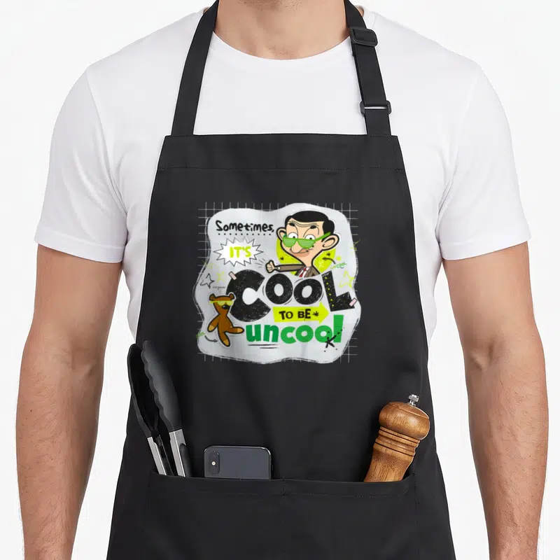 Uncool mr apron - Cartoon man with green sunglasses and brown teddy bear with yellow glasses on grid background — shown on a black cotton canvas apron against a white background