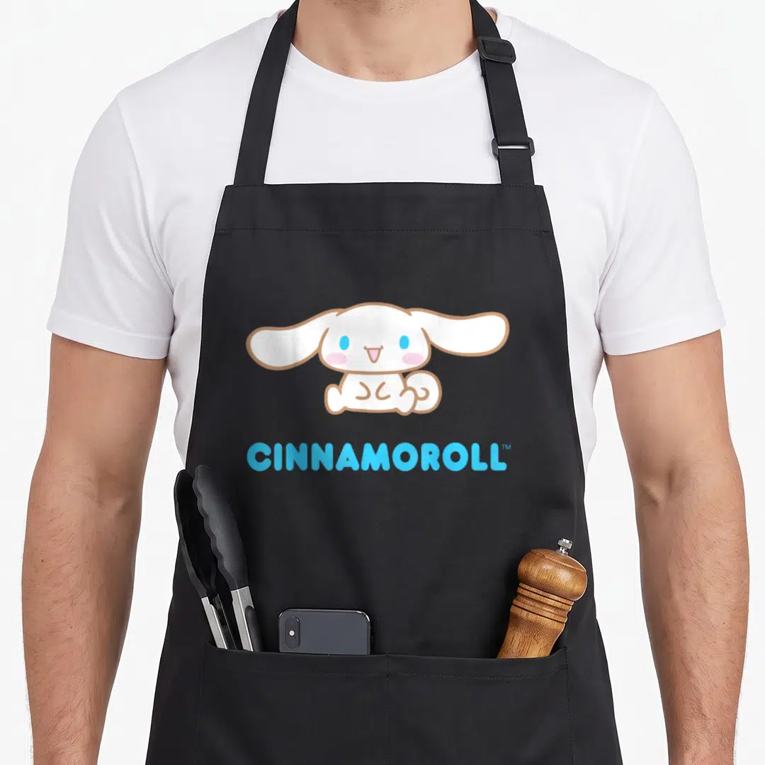 Character cinnamoroll apron - White cartoon dog with blue eyes above light blue CINNAMOROLL text — shown on a black cotton canvas apron against a white background