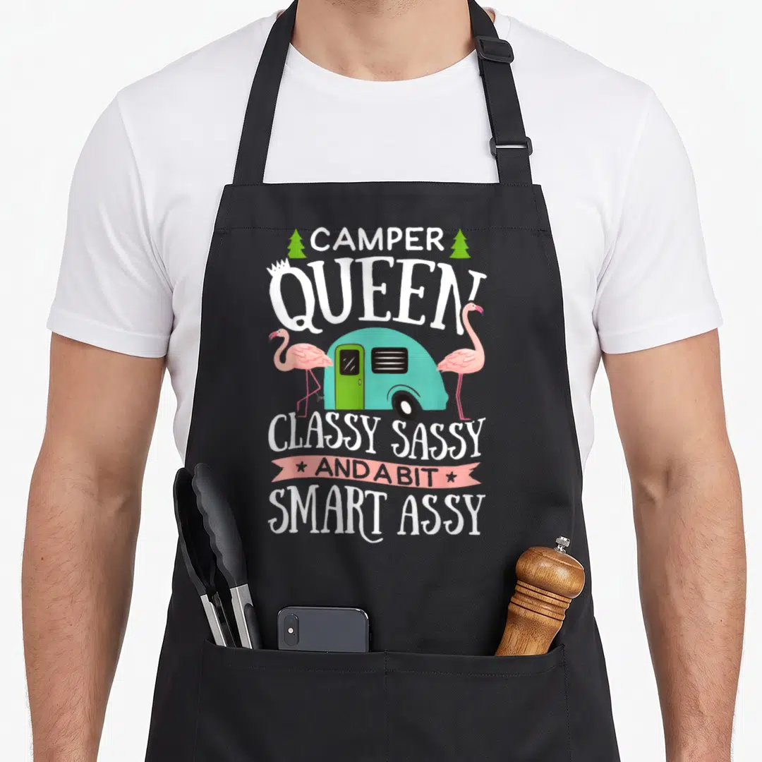 Camper smart apron - Teal camper van flanked by two pink flamingos under stacked white text reading Camper Queen Classy — shown on a black cotton canvas apron against a white background