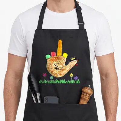 Friendsgiving pilgrim apron - Cartoon turkey in top hat with red, yellow, green, and red tail feathers standing on grass — shown on a black cotton canvas apron against a white background