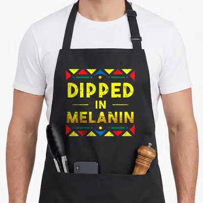 Dipped african apron - DIPPED IN MELANIN text surrounded by red, yellow, blue, and green geometric triangles — shown on a black cotton canvas apron against a white background