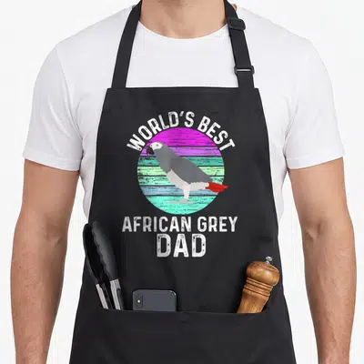 African bird apron - Cartoon grey parrot on pink teal striped circle with World's Best African Grey Dad text — shown on a black cotton canvas apron against a white background