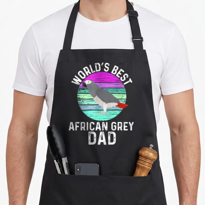 African bird apron - Cartoon grey parrot on pink teal striped circle with World's Best African Grey Dad text — shown on a black cotton canvas apron against a white background