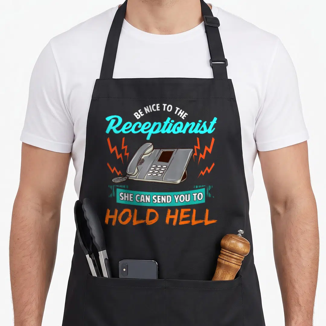 Call receptionist apron - Grey phone flanked by orange bolts with text Be Nice To The Receptionist She Can Send You — shown on a black cotton canvas apron against a white background