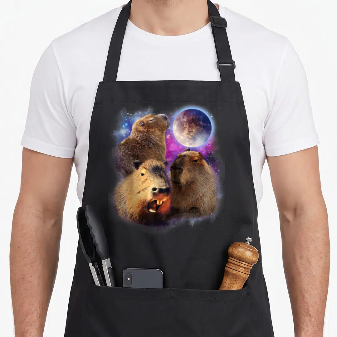 Stuffed animal apron - Three realistic capybaras under a moon with purple blue grey nebula — shown on a black cotton canvas apron against a white background