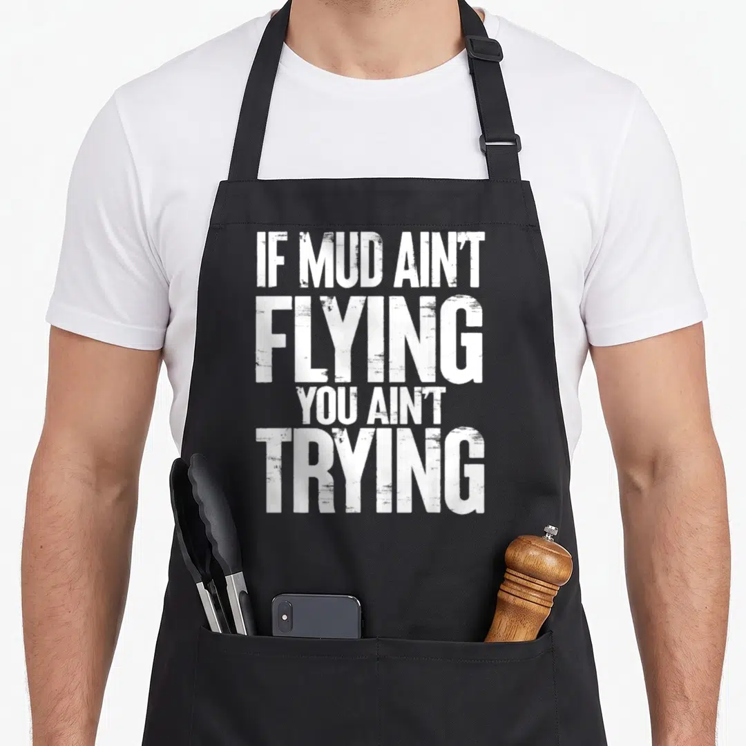 Four atv apron - White stacked typography reading IF MUD AIN'T FLYING YOU AIN'T TRYING — shown on a black cotton canvas apron against a white background