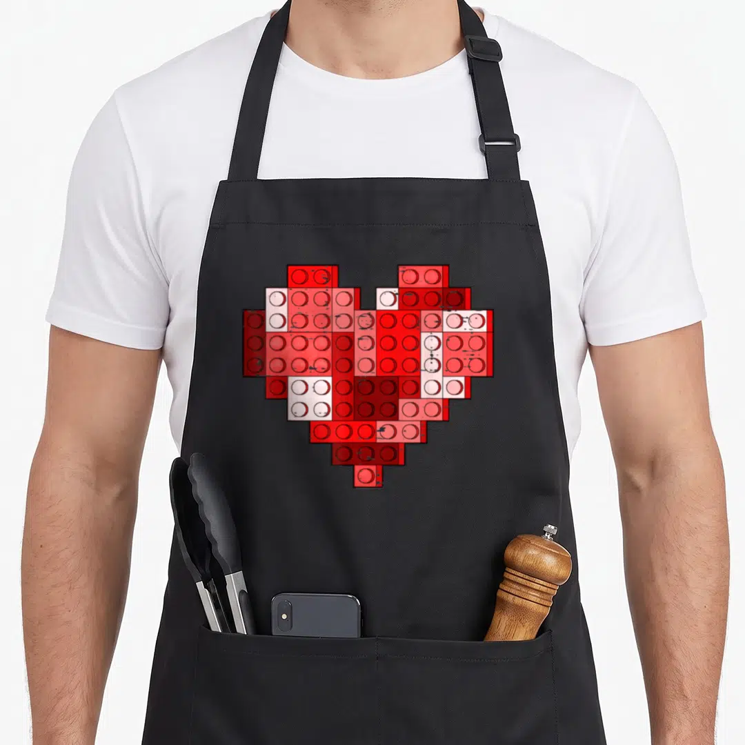 Valentine building apron - Heart shape formed by cluster of red plastic bricks in varying shades — shown on a black cotton canvas apron against a white background