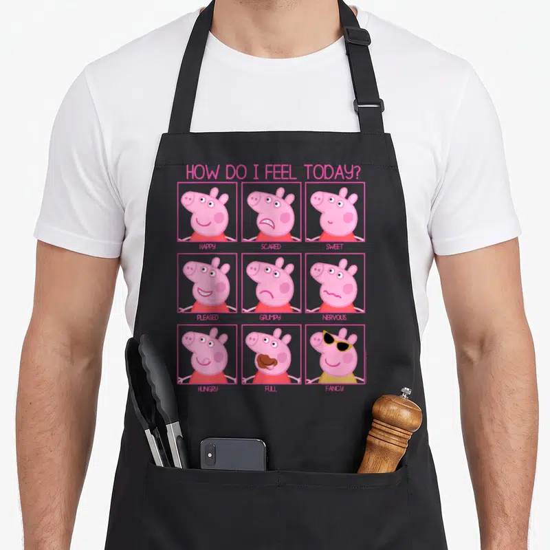 Feel crazy pig man apron - Peppa Pig 3x3 grid faces labeled happy scared sweet pleased grumpy nervous hungry full fancy — shown on a black cotton canvas apron against a white background