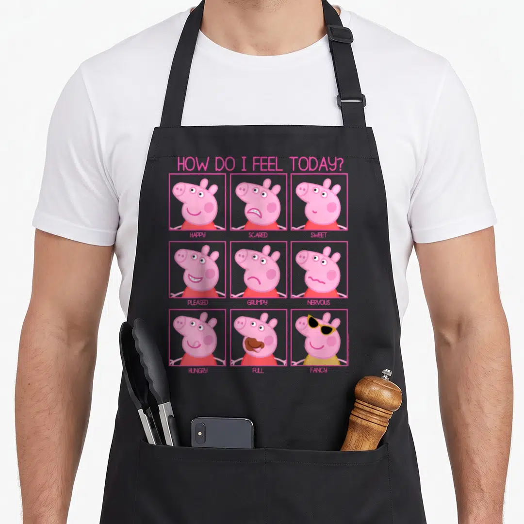 Feel crazy pig man apron - Peppa Pig 3x3 grid faces labeled happy scared sweet pleased grumpy nervous hungry full fancy — shown on a black cotton canvas apron against a white background