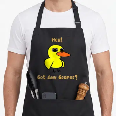 Cafepress lemonade apron - Yellow cartoon duck with orange beak between text Hey! and Got Any Grapes? — shown on a black cotton canvas apron against a white background