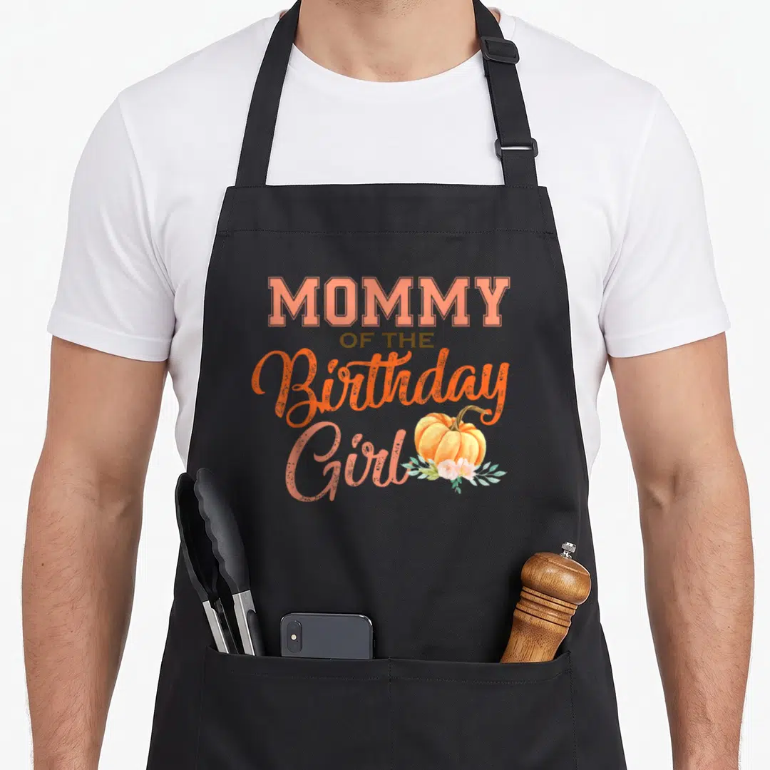 Pumpkin funny halloween apron - Stacked MOMMY OF THE Birthday Girl text with pumpkin and floral accents — shown on a black cotton canvas apron against a white background