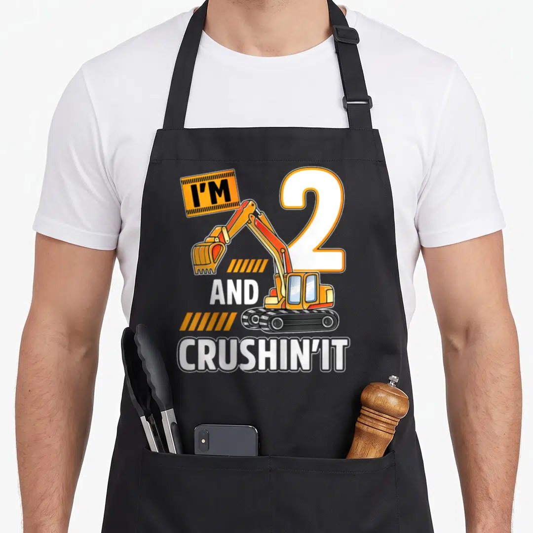 Vehicle 2nd apron - Cartoon excavator holding I'M sign next to number 2 with orange stripes and white text — shown on a black cotton canvas apron against a white background