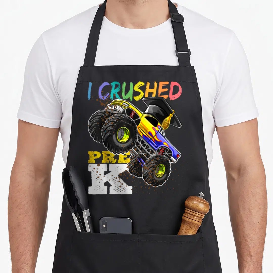 Pre truck apron - I Crushed Pre K monster truck with graduation cap and mud splatters — shown on a black cotton canvas apron against a white background