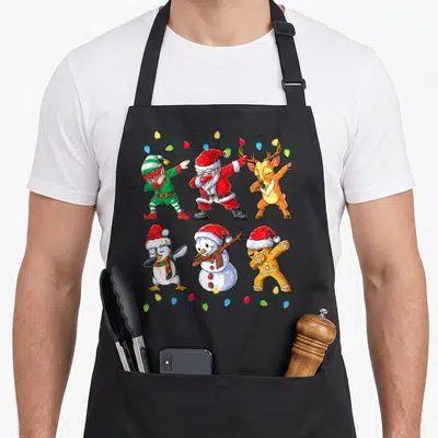 Dabbing christmas elf apron - Six cartoon Christmas characters dabbing under string lights in red green and brown — shown on a black cotton canvas apron against a white background