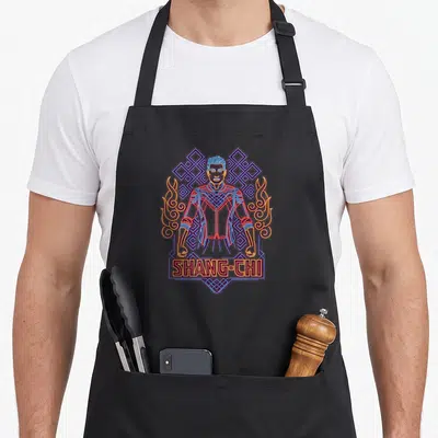 Legend ring apron - Neon line art of a man with blue geometry, yellow flames, and SHANG-CHI text in a box — shown on a black cotton canvas apron against a white background