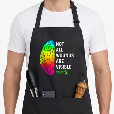 Wound anesthesiologist problems apron - Rainbow half-brain next to stacked white text reading Not All Wounds Are — shown on a black cotton canvas apron against a white background