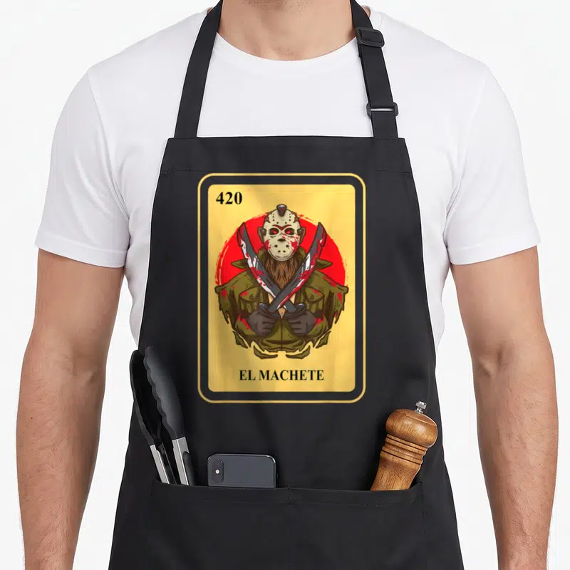 Machete bingo aprons - Cartoon Jason Voorhees holding two crossed machetes inside yellow frame with 420 EL MACHETE text — shown on a black cotton canvas apron against a white background