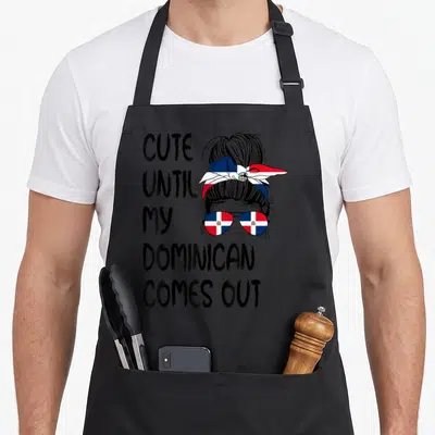 Come dominican apron - Cartoon woman with messy bun, flag headband, and sunglasses next to stacked text — shown on a black cotton canvas apron against a white background