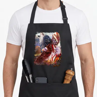 Wolf bald american flag apron - Realistic wolf howling behind flying eagle with USA flag wings over rocky mountains — shown on a black cotton canvas apron against a white background