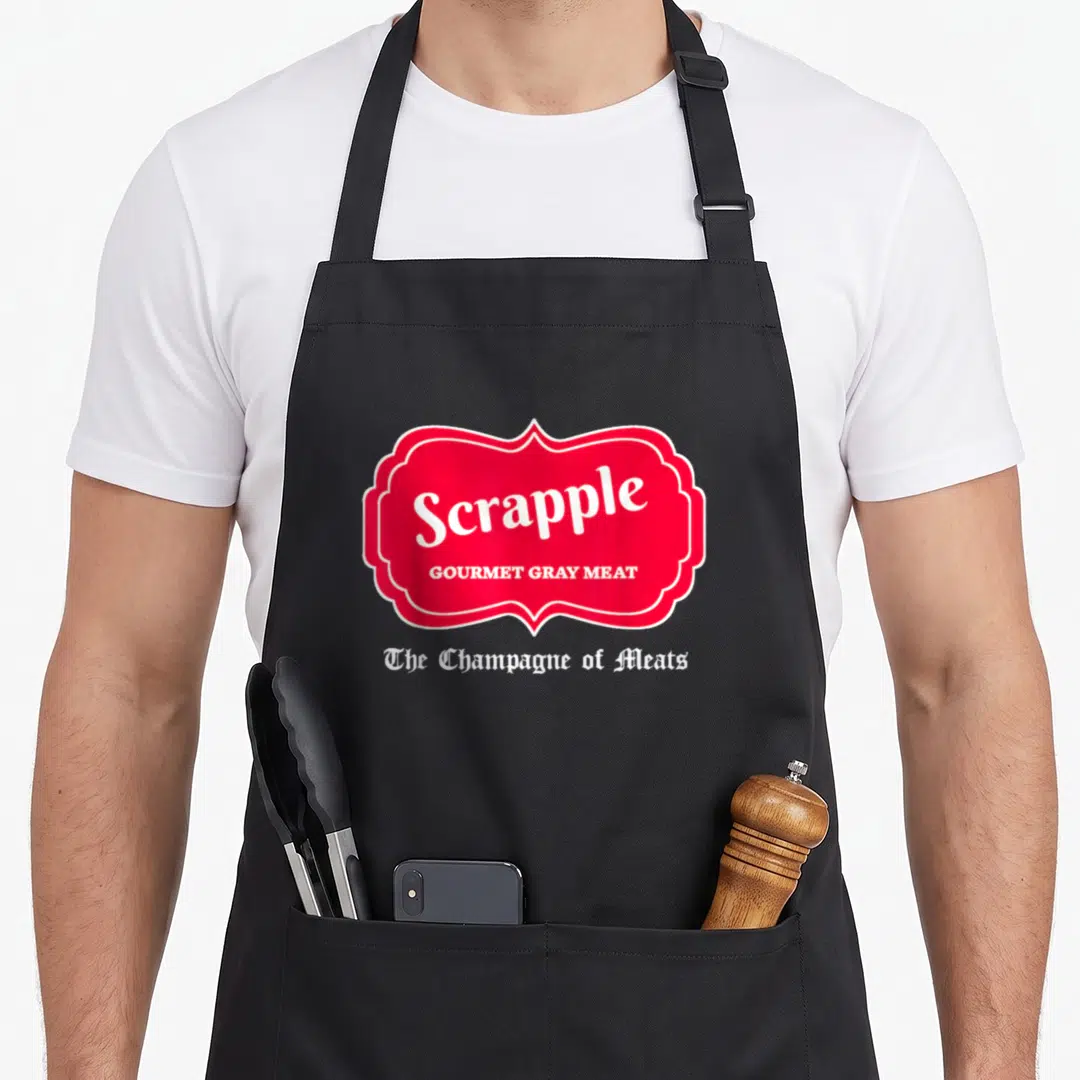 Scrapple champagne apron - Red label reading Scrapple Gourmet Gray Meat with white gothic text below on gray background — shown on a black cotton canvas apron against a white background