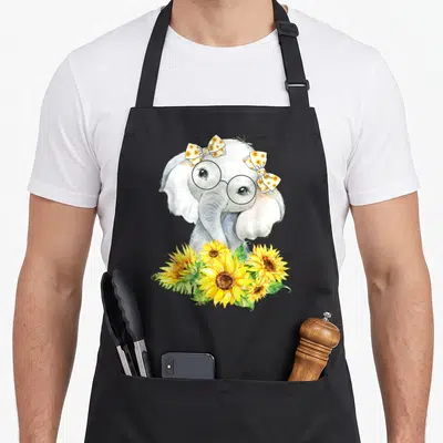 Funny elephant sunflower apron - Grey elephant with glasses and two sunflower bows above yellow flowers in watercolor — shown on a black cotton canvas apron against a white background