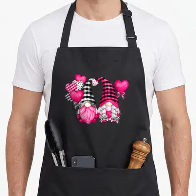 Balloon buffalo apron - Two gnomes with pink and black plaid hats forming a heart surrounded by patterned balloons — shown on a black cotton canvas apron against a white background