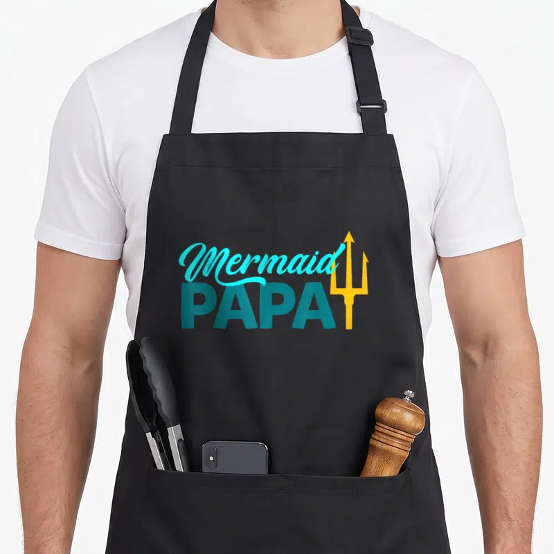 Security grandpa apron - Mermaid PAPA text in cyan and teal with a yellow trident standing vertically beside it — shown on a black cotton canvas apron against a white background