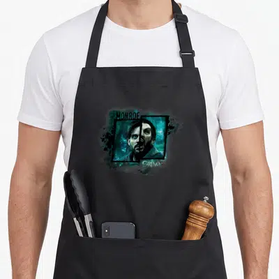 Nbc christmas apron - Split face man monster print with MONROE and GRIMM text in teal black white — shown on a black cotton canvas apron against a white background