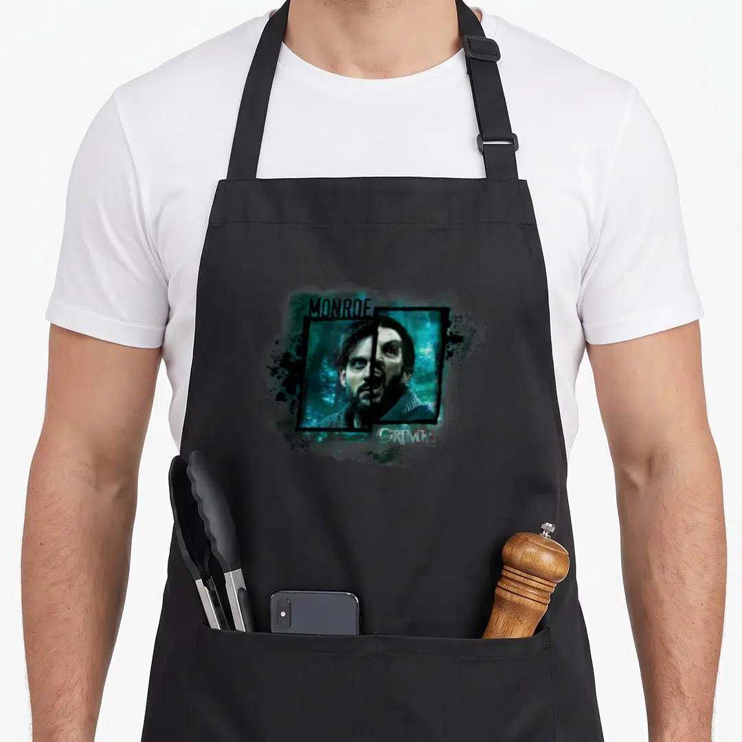 Nbc christmas apron - Split face man monster print with MONROE and GRIMM text in teal black white — shown on a black cotton canvas apron against a white background