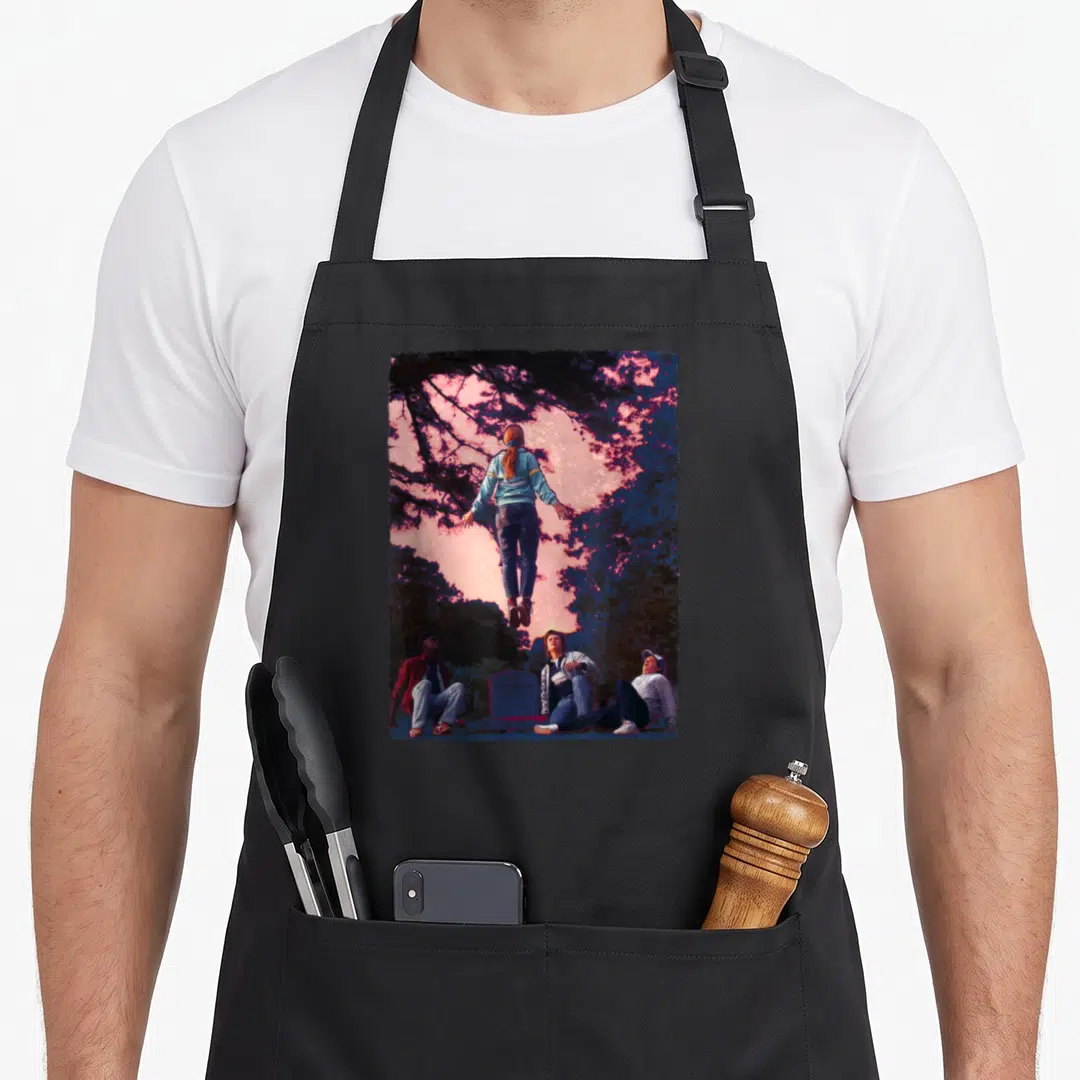 Max mad apron - Girl floating above three boys under pink and purple sky with tombstone — shown on a black cotton canvas apron against a white background