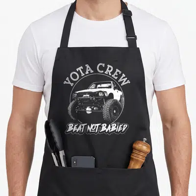 4x4 road apron - White distressed truck in circle with YOTA CREW and BEAT NOT BABIED text — shown on a black cotton canvas apron against a white background