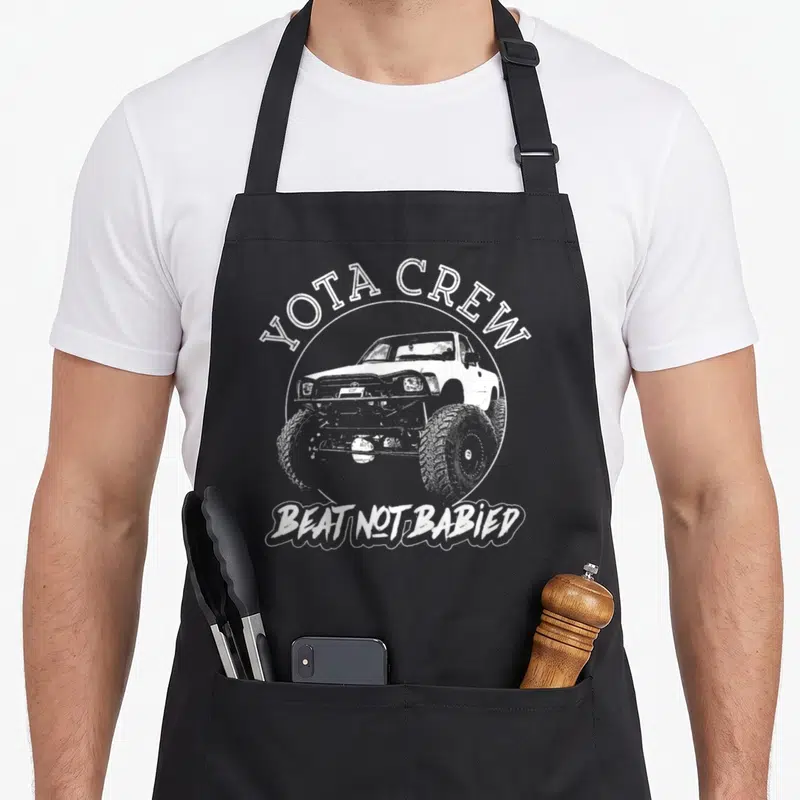 4x4 road apron - White distressed truck in circle with YOTA CREW and BEAT NOT BABIED text — shown on a black cotton canvas apron against a white background